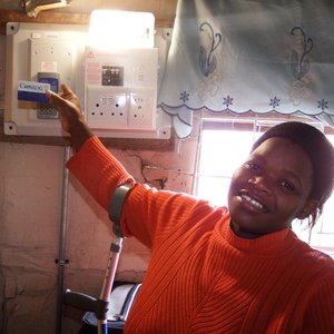 â€˜n Vreugdevolle gestremde Bukelwa Mbuzweni by haar elektrisiteitstoestel vir elektrisiteit in haar woning